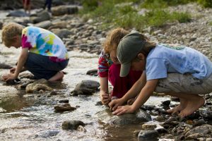 Niños tocando las rocas de un río; aprendizaje y tacto